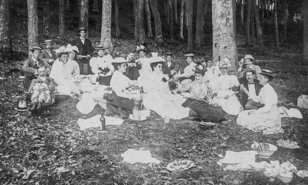 Group of Victorian-era men and women having a summer picnic in the woods.