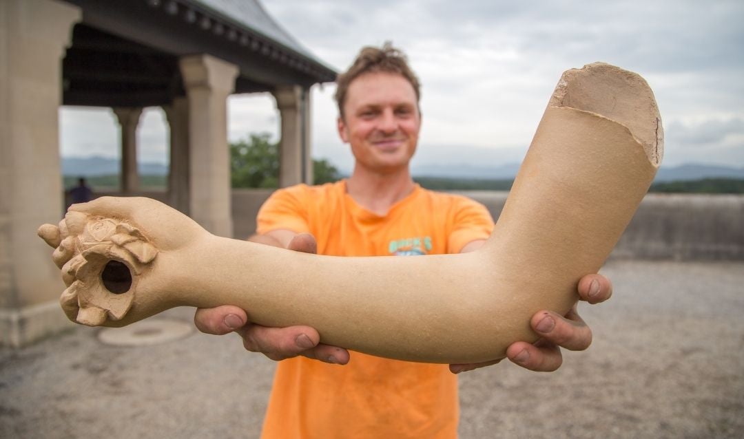 Artist holds up the replacement arm for the statue of Flora.