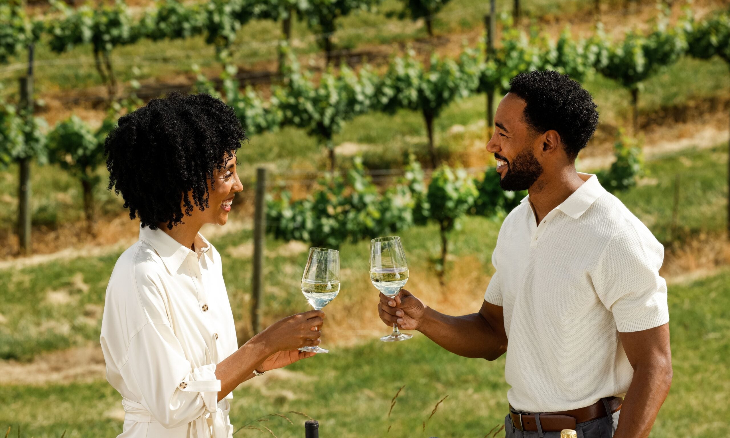 Man and woman toast with white wine at a summer white party in a vineyard.