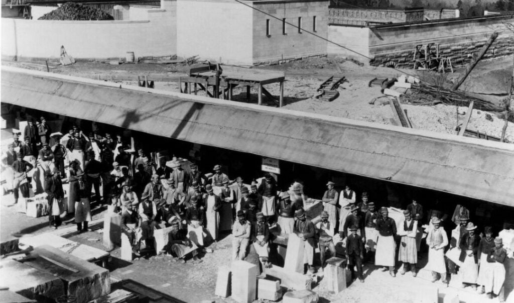 Archival photo of stonemasons with blocks of limestone in the stonecutting sheds on the Esplanade during Biltmore House construction