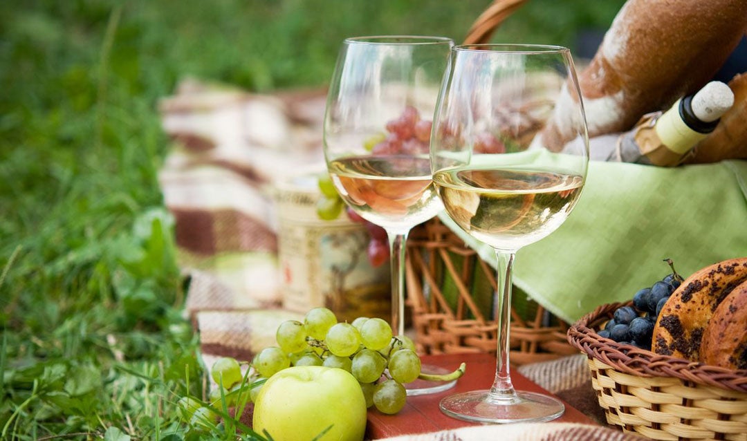 Two glasses of white wine with fruit and a basket.