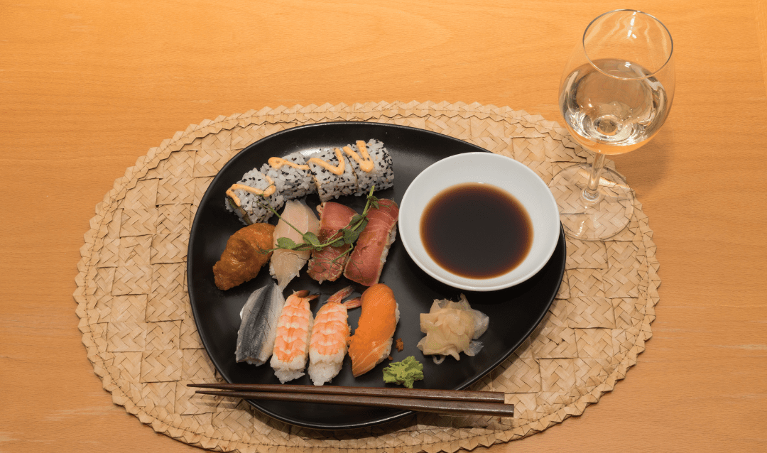 Glass of white wine with sushi on a black plate.