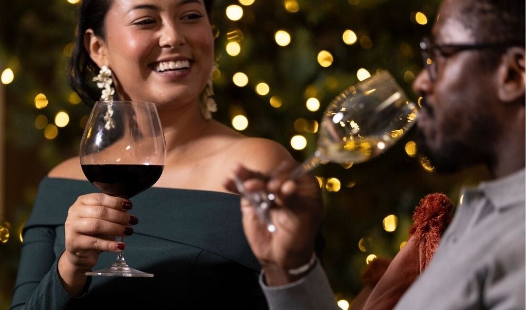 Man and woman drinking wine in front of Christmas lights.