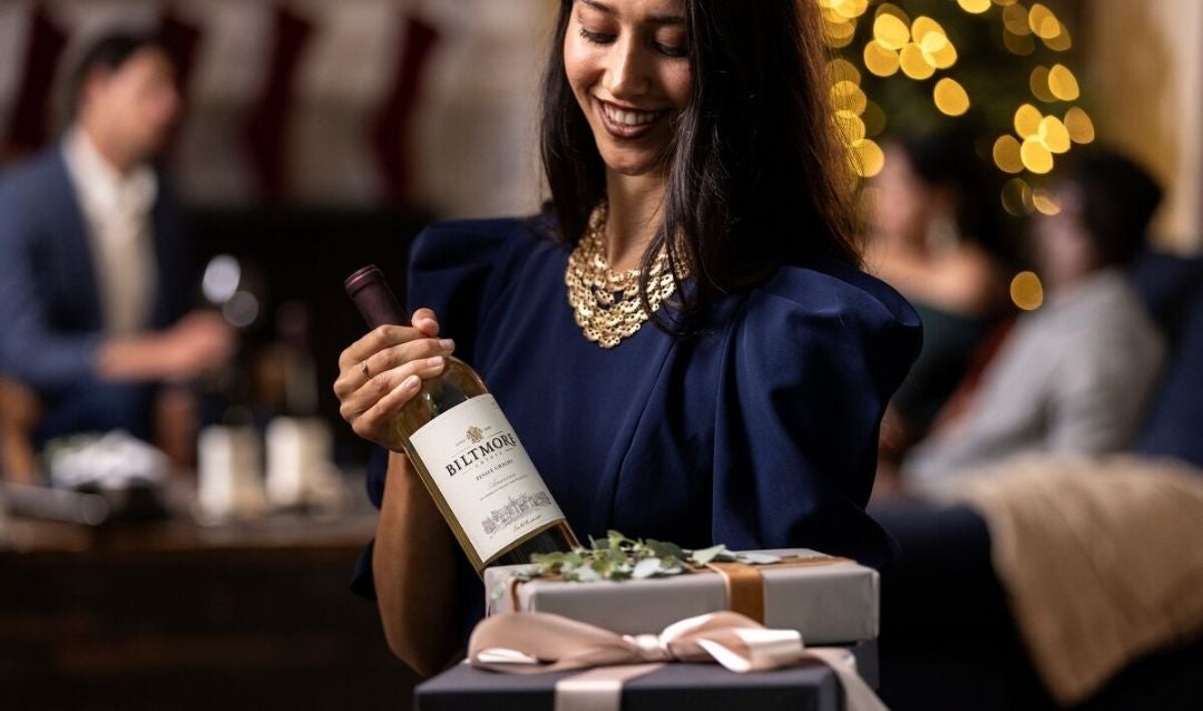 Woman holding a bottle of Biltmore Estate Chardonnay and Christmas gifts.