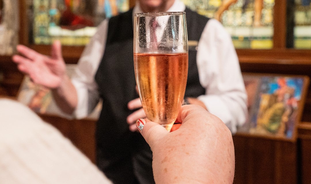 Person holding a flute of pink sparkling wine.
