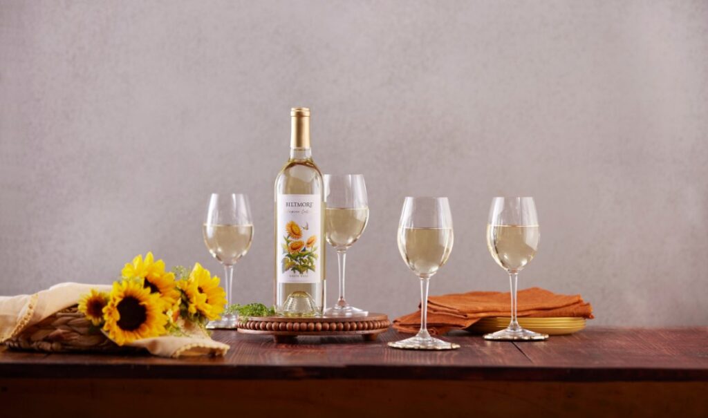A bottle of Biltmore Masterpiece Collection White Wine with four glasses and a bouquet of sunflowers.
