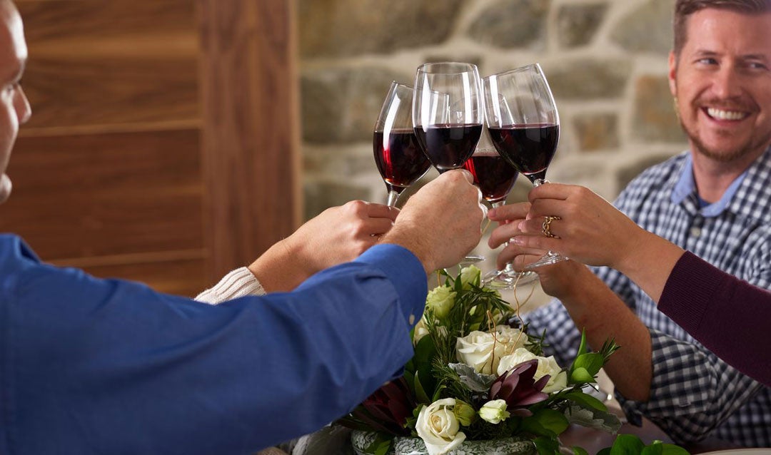 Four people toasting with glasses of red wine.