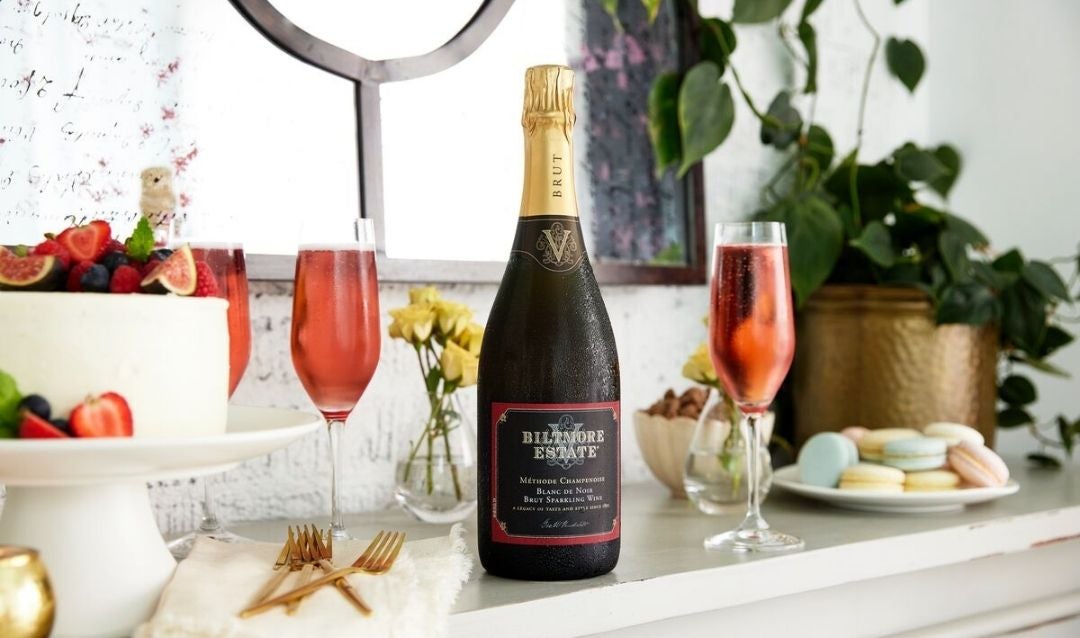 Bottle of Biltmore Estate Blanc de Noir and several flutes of wine on a sideboard.