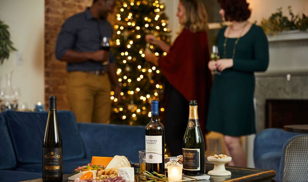 Three friends in front of a Christmas tree with Biltmore wines and charcuterie