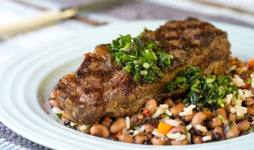 Steak and black-eyed peas with chimichurri sauce on a plate.