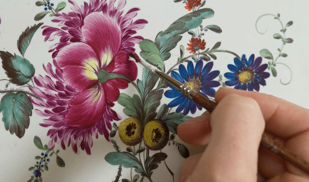 A conservator repaints flowers on ceramic tiles with a tiny brush