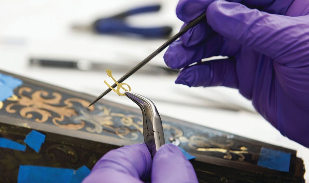 A staff member is preserving and restoring brass inlay to a desk in Biltmore House