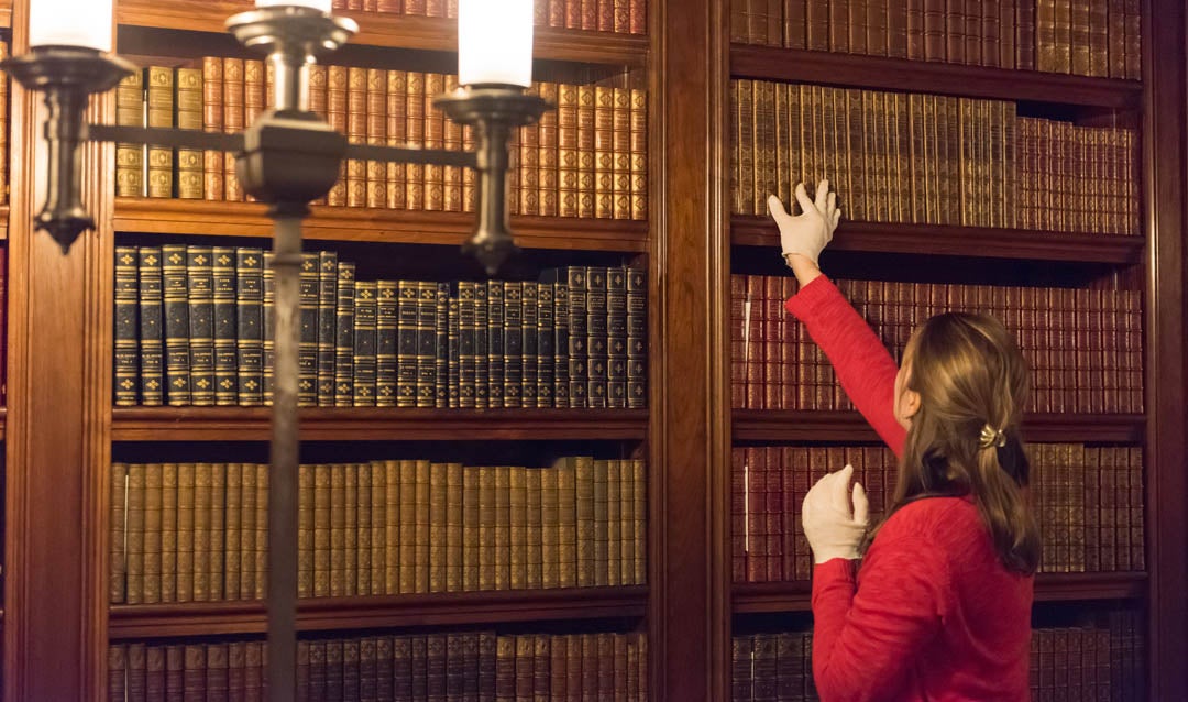 Associate curator Lauren Henry inspects books in the Biltmore House Library. Topics in George Vanderbilt’s personal collection range in subject from American and English fiction to world history, religion, philosophy, art, and architecture.