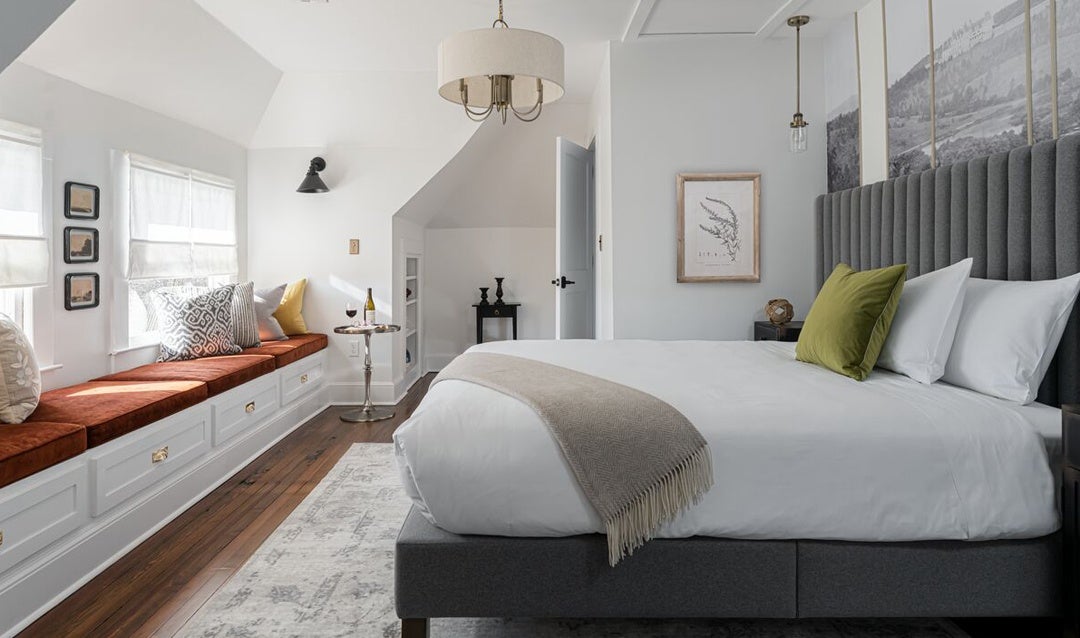 The upstairs bedroom boasts double-window seating with ample natural light to illuminate the vintage Biltmore photographs displayed above the upholstered headboard.