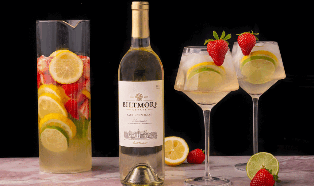 Bottle of Biltmore Estate Sauvignon Blanc and glasses of sangria with fruit garnish.