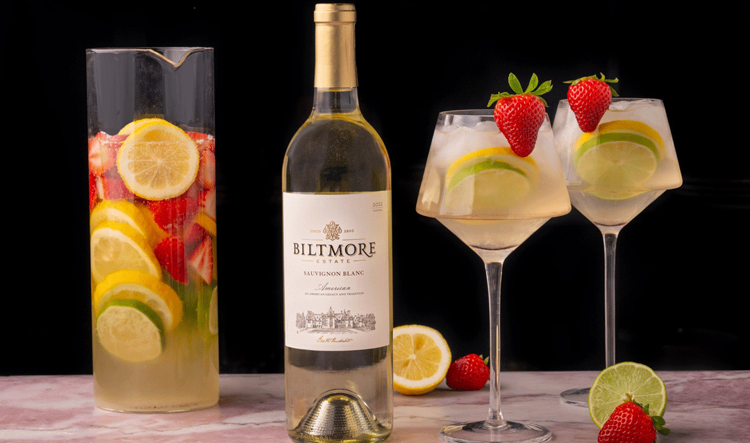 Bottle of Biltmore Estate Sauvignon Blanc and glasses of sangria with fruit garnish.