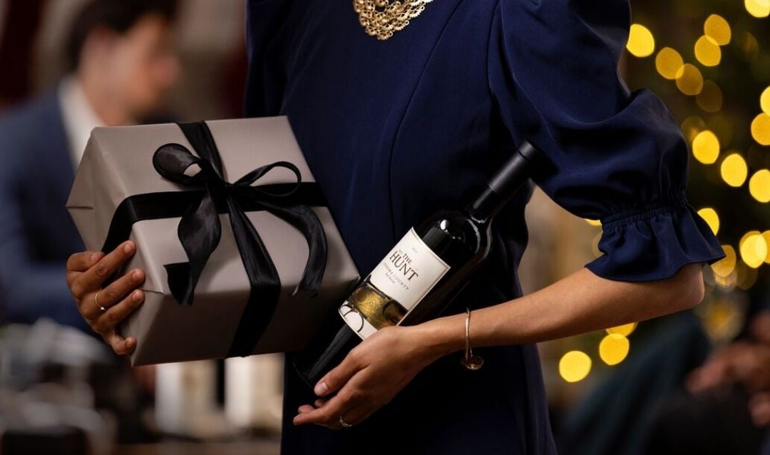 Woman holding a gift-wrapped package and a bottle of Biltmore wine.