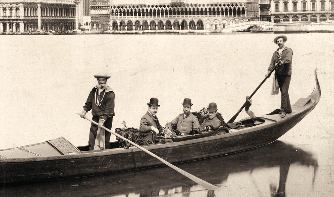 Archival photo of three passengers and two rowers in a gondola in Venice, Italy