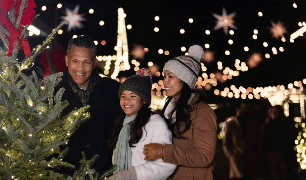 Smiling family in winter clothes looks at lighted outdoor Christmas tree