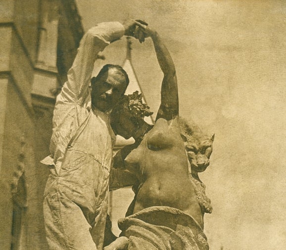 Samuel Isaac Bean (a white man) poses with a sculpture outside Biltmore House. He holds the female sculpture’s hands as if dancing with it.