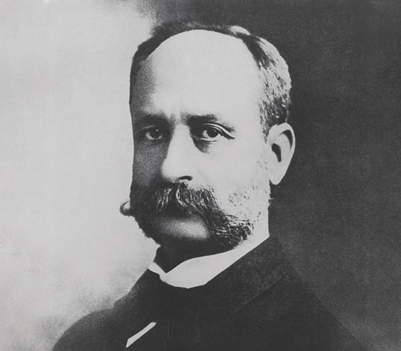 Rafael Guastavino (a white man) poses for a portrait wearing a white shirt under a dark suit. He has a thick mustache and dark eyes.