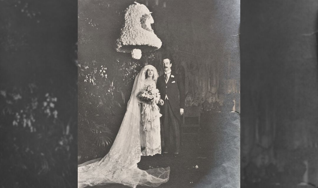 The Honorable and Mrs. John F.A. Cecil pose beneath a large wedding bell displayed in the Tapestry Gallery.