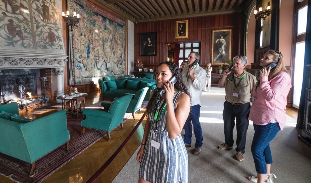 Group of men and women listening to an audio tour in the Tapestry Gallery of Biltmore House.
