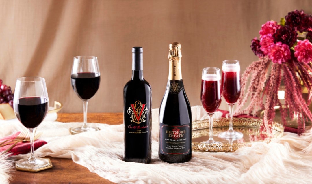 Two bottles of red Biltmore wine with filled glasses.