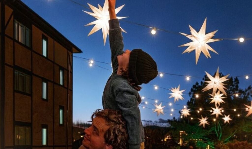 Boy reaching for lighted Moravian stars while seated on a man's shoulders in Antler Hill Village at Biltmore Estate