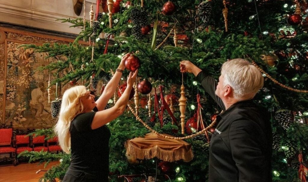 Two people decorate the Banquet Hall Christmas tree at Biltmore