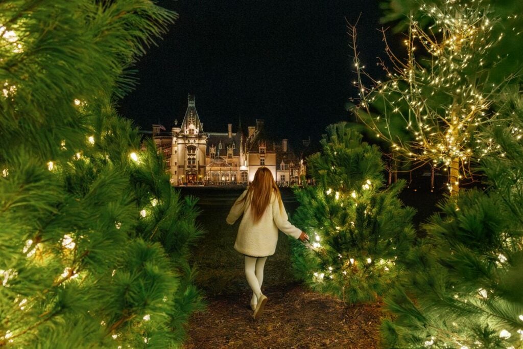 A child runs through the lighted evergreen trees in front of Biltmore House during Candlelight Christmas Evenings