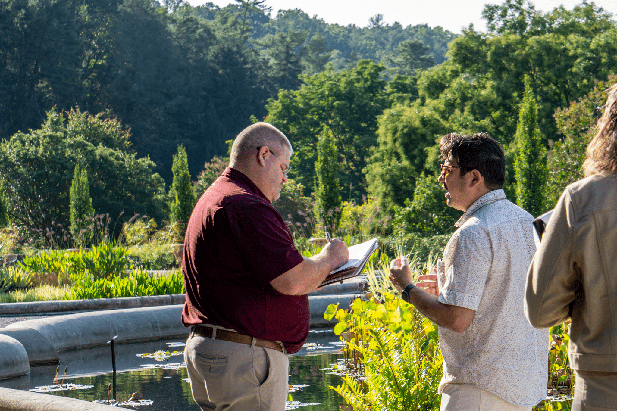 Two men talking and taking notes in a garden area.