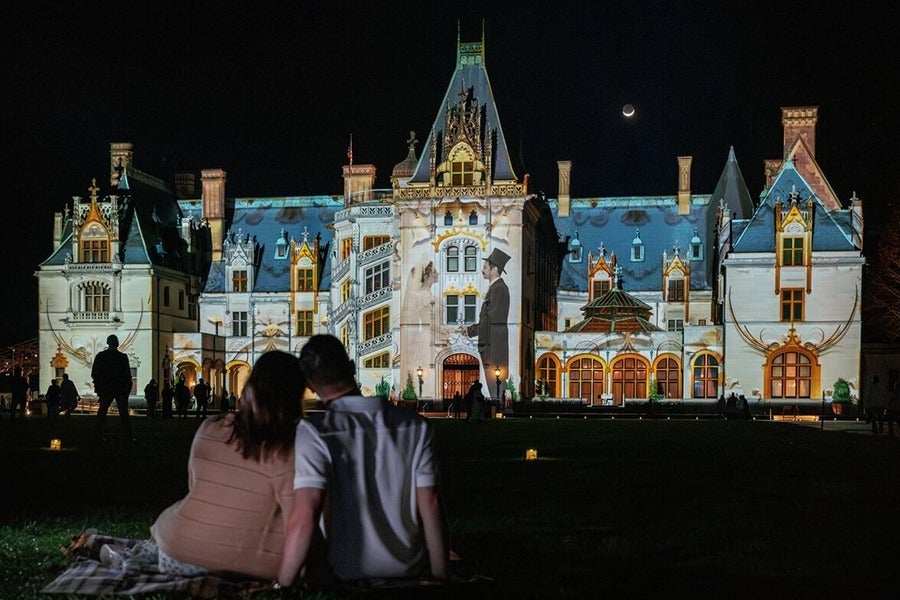 couple sitting on Front Lawn at night enjoying Luminere show on Biltmore House facade
