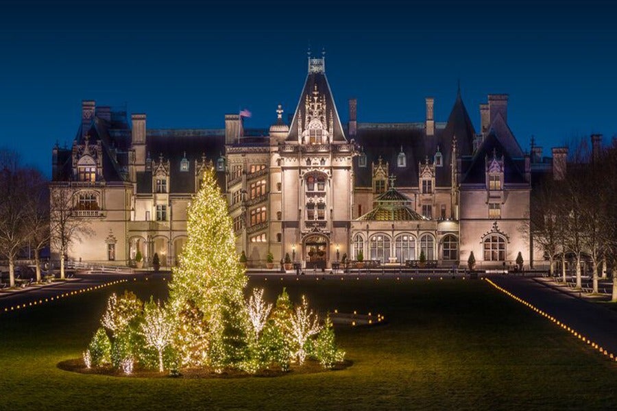 Biltmore House facade and front lawn trees glow at night during Candlelight Christmas